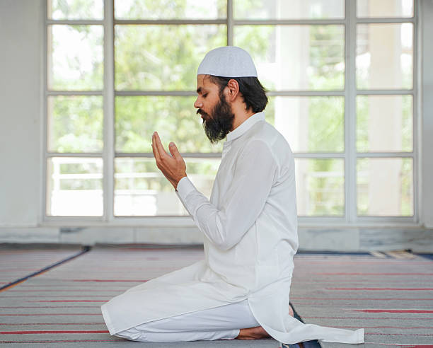istock Devout Muslim man in white kneels in prayer inside a mosque, raising hands in supplication with eyes closed. 2217495245