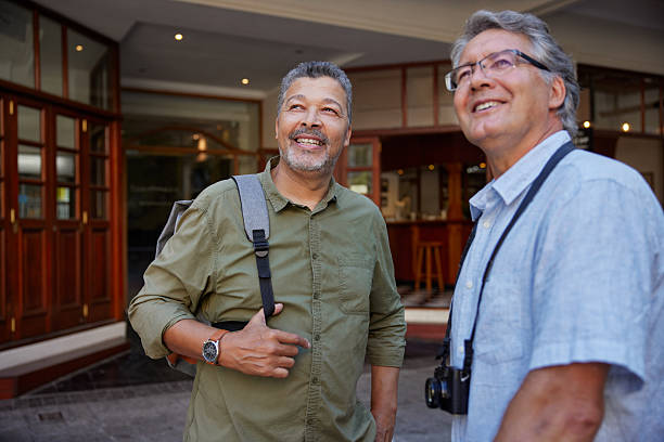 Two happy smiling men look up while exploring the city together during a vacation. Older male friends sightseeing and enjoying their time outside. Smiling and happy  men looking away during their walk.