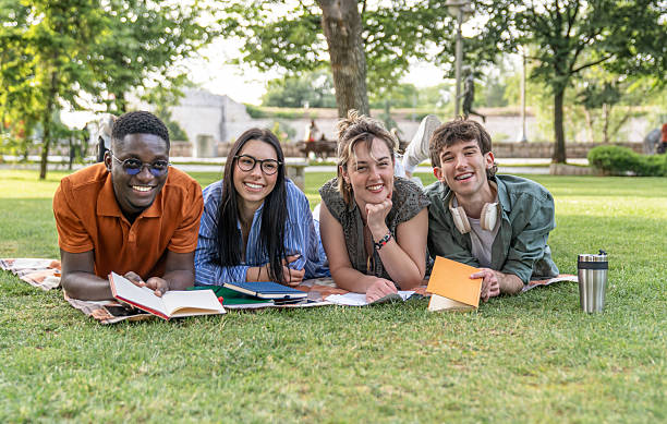 istock Cheerful students lying on grass reading books in park 2217502154
