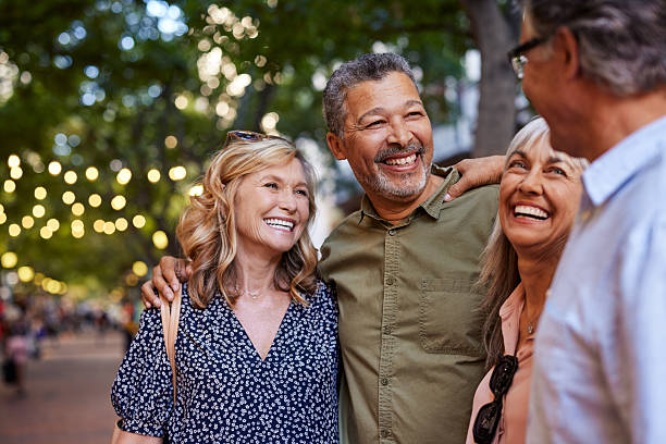 Mature women and men laughing together Group of happy senior friends sharing a moment outdoor while embrace. Older men and laughing women chatting together during a walk. Close up face of cheerful retirees enjoying time in a lively city street. friendship stock pictures, royalty-free photos & images
