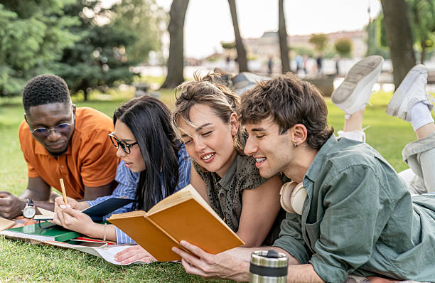 istock Students lying on grass reading and studying together in a park 2217503036
