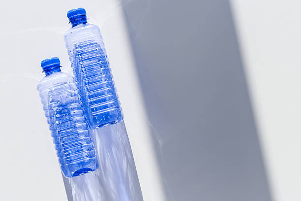 istock Clear plastic water bottles for clean water on white blue background closeup, minimal aesthetic lifestyle photo, top view, flat lay, Naural light, sunlight shadows, caustic light effect, star filter 2217515459