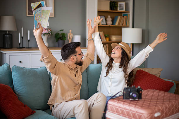 Young couple celebrating planned trip with raised arms and maps
