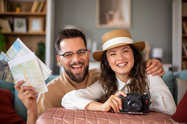 istock Young couple smiling and holding maps and camera, planning a trip 2217522322