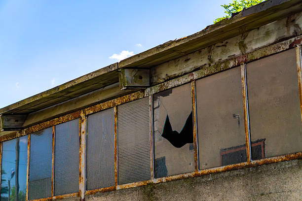 Damaged window with broken glass in a neglected industrial structure. Rusty frames and signs of decay are clearly visible.