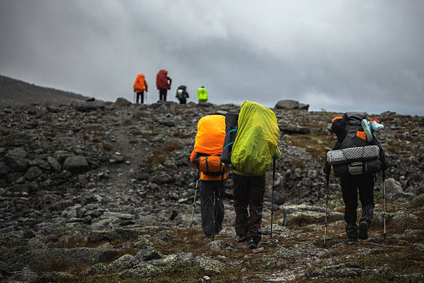 A group of hikers trekking uphill on a rugged trail under a cloudy sky, carrying backpacks and hiking gear, showcasing adventure, travel, and exploration in a natural outdoor setting.