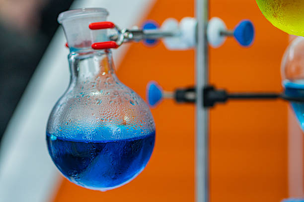 Retort stand and laboratory flask with liquid on white background, closeup. Space for text
