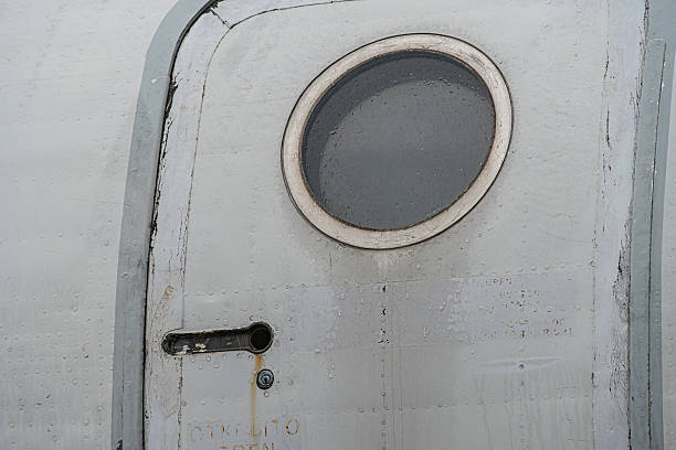 istock Close-up view of an aged airplane side, featuring a porthole window with handle and latches, diffused light, subtle wear and shadows 2217531097