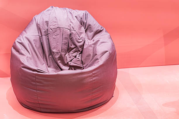 Portrait of elementary schoolgirl relaxing on bean bag with classmates in background. Cute girl sitting on bean bag at school and looking at camera.