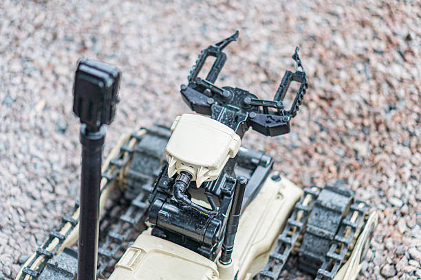 A robotic exploration vehicle is shown on an outdoor surface, equipped with multiple limbs and a camera or sensor device The robot has a rugged design, gray-brown color scheme, and industrial appear