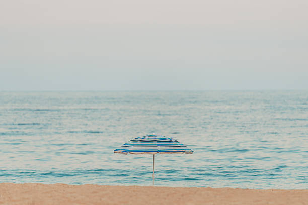 Lonely sun umbrella parasol at sandy beach on overcast summer day, selective focus