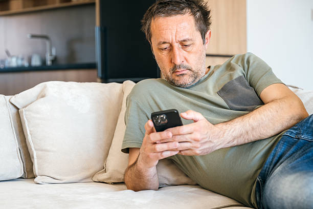 istock Bored couch potato guy using mobile phone while laying on living room sofa 2217532858