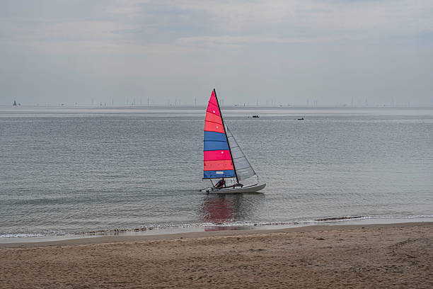 A small catamaran sails along the beach in Brittany
