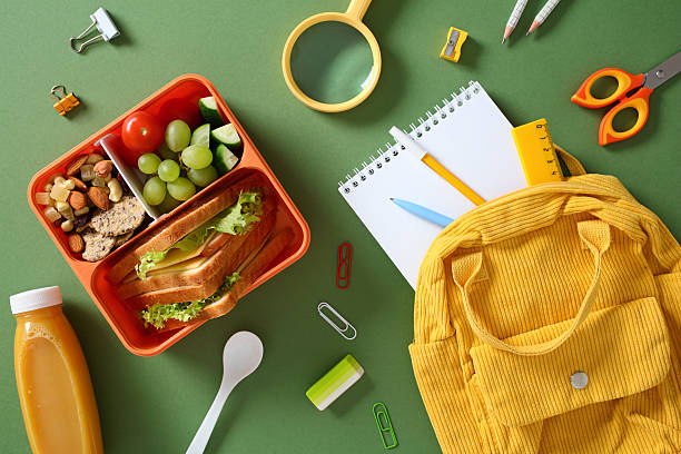 istock Healthy packed lunch for students: bento box with sandwich, grapes, and snacks, with school supplies and backpack. 2217536094