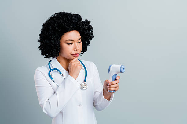 A young medical professional in a white lab coat examines a diagnostic tool, demonstrating focus and consideration, against a neutral gray background.