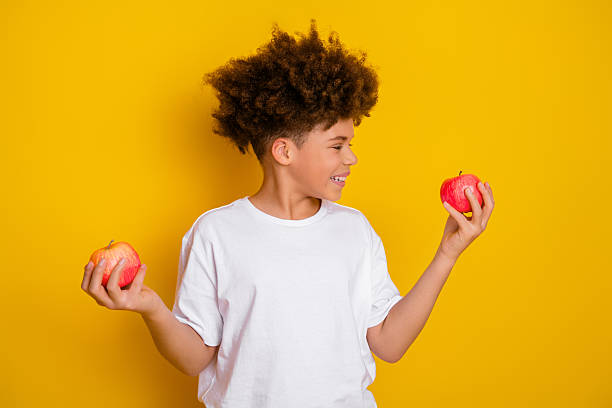 istock Young boy holding apples in both hands against a bright yellow background, expressing cheerful style and healthy lifestyle vibes 2217536557