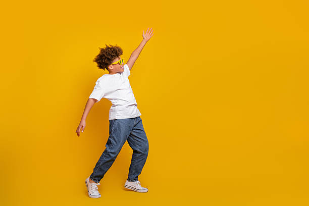 istock Trendy boy in casual attire making dynamic gestures against vibrant yellow background 2217536573