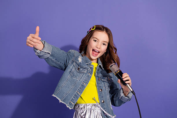 istock Charming young girl singing into a microphone against a vibrant violet background showcasing stylish casual fashion 2217536740