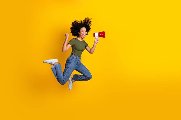 istock Excited young woman jumping high while shouting through a megaphone against a vibrant yellow background 2217537048
