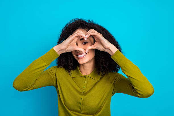 istock Charming young woman smiling joyfully, gesturing heart with hands against vibrant blue background. 2217537109