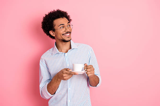 istock Stylish young man with glasses holding a coffee cup against a pink backdrop, showcasing elegance and casual leisure. 2217538468