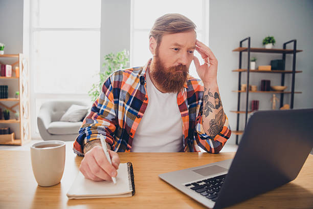 istock Bearded Man Working on a Laptop and Writing Notes at a Desk in a Bright Home Interior 2217538894