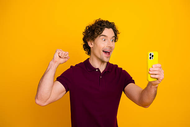 istock Excited young man celebrating success while looking at phone in vibrant yellow background 2217538983
