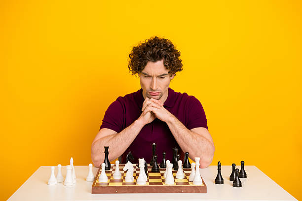 Thoughtful gentleman focusing on a chess game against a bright yellow background with a stylish and relaxed demeanor