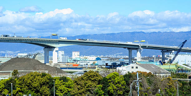 Osaka, Japan - April 15, 2052: Looking north from Route 2 in Hokuko, Konohana Ward. Route 5 spans the Shorenji River and continues toward Kobe in Hyogo Prefecture. Spring morning with clouds above Osaka Bay.