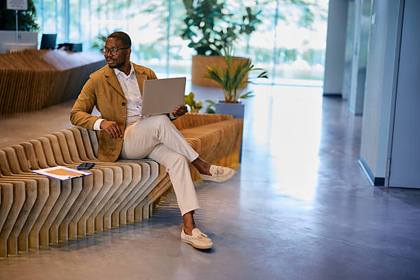 istock Businessman working on laptop while sitting on bench in modern office lobby 2217544425