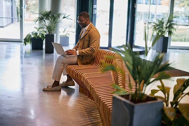 istock Businessman working on laptop sitting on modern bench in office lobby 2217544458