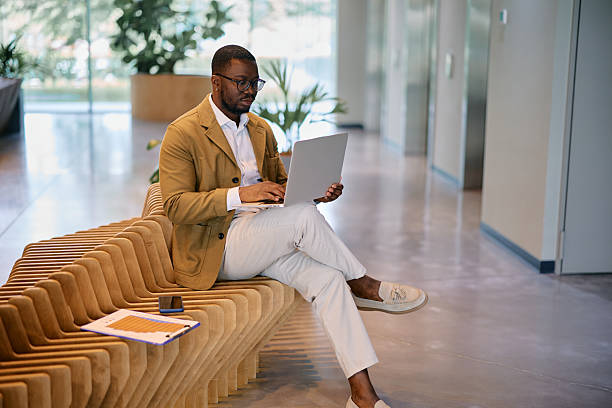 istock Businessman working on laptop while sitting on bench in modern office lobby 2217544459