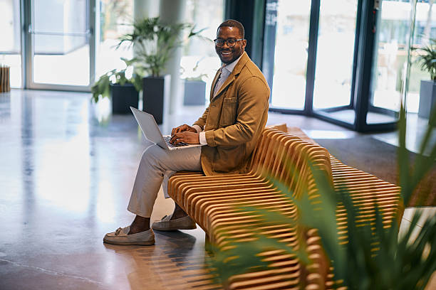 istock Businessman working on laptop while sitting on bench in modern office lobby 2217544460