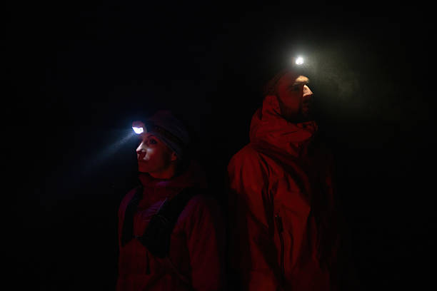 Couple equipped with headlamps explore a forest in total darkness, with beams of light cutting through the night air.