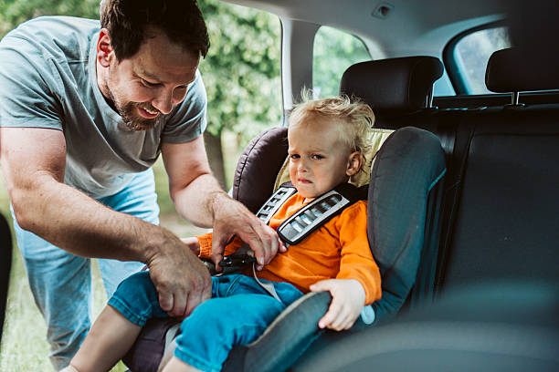 istock Toddler frowns while dad buckles him into car seat. 2217545332