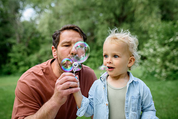 istock Father and son blowing soap bubbles in park. 2217545659