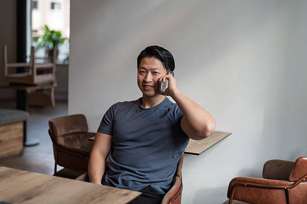 istock Young asian man talking on phone, sitting at empty table. 2217546480