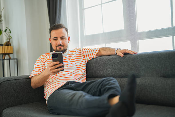 istock Man lying on sofa in living room looking at mobile phone 2217546570