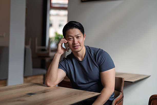 istock Young asian man talking on phone, sitting at empty table. 2217546624