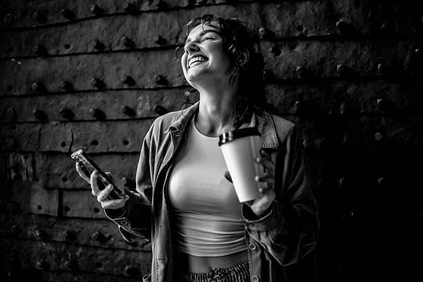 Black and white photo of a cheerful woman holding a coffee cup and smartphone, radiating joy and positivity, set against a textured background.