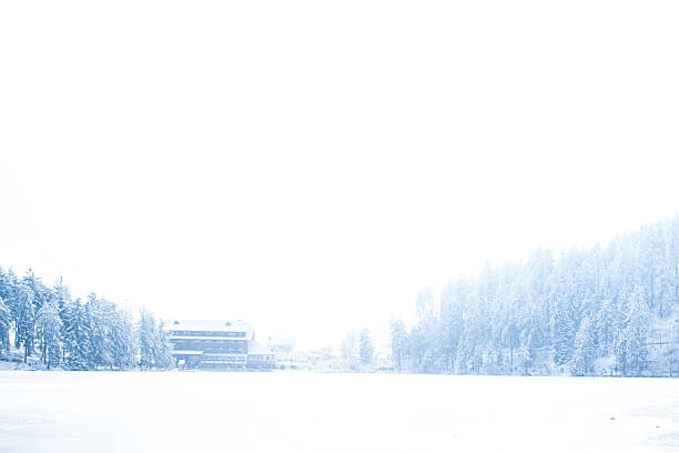 A serene winter landscape of Mummelsee, a famous lake in the Black Forest, Germany, captured under a blanket of snow. The frozen lake reflects the surrounding snow-draped pine trees and a charming wooden lodge on the shore. The overexposed, dreamy atmosphere enhances the sense of calm and cold, making this an ideal scene of a peaceful winter wonderland.