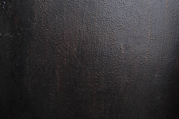Detailed view of dark, heavily textured material, possibly paint or a coating, showing a rough surface with many small bumps and varied light play.