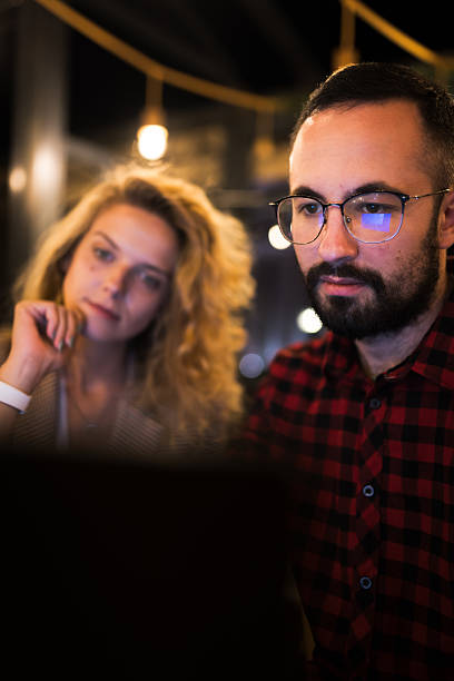 istock Focused team collaboration session with two colleagues working together on a laptop at night in a modern office. Intense problem-solving and brainstorming atmosphere with business professionals in casual attire. 2217561840