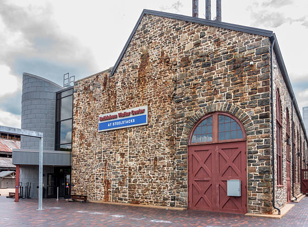 Bethlehem, PA - US - May 25, 2025 Closeup of the old stone Bethlehem Visitor Center at SteelStacks, featuring a bold red wooden door, stands proudly under towering stacks and a dramatic sky.