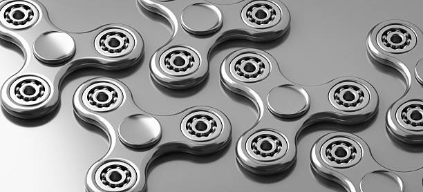This Modern Art Illustration presents a Close-Up Top Down View of multiple Metallic Silver - Metal or Gray Color Fidget Spinner Toys arranged in a Pattern. The Shiny surfaces and visible Ball Bearings highlight the Mechanics and Precision of these objects. This Abstract Concept Design evokes themes of Repetition, Leisure Activity, and potential Stress Relaxation. The image reflects a Modern Period Childhood trend and can be associated with Hobbying, Playful Fun, or simply the Motion of Spinning. It is a Still Life that captures both Simplicity and Industrial Design elements within its Organization.