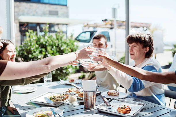 A group of teenagers toast with water glasses while having lunch together on the patio of a pizzeria on a sunny afternoon in Washington State.