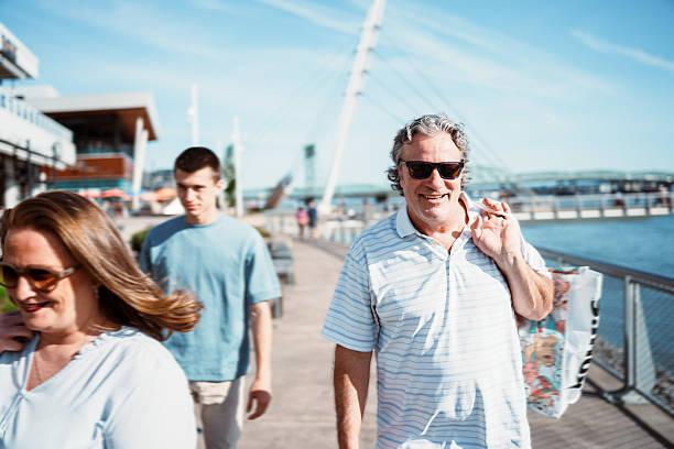 A man smiles while walking with his wife and teenage son on a pedestrian path along the Columbia River while spending the afternoon in downtown Vancouver, Washington on a sunny day.