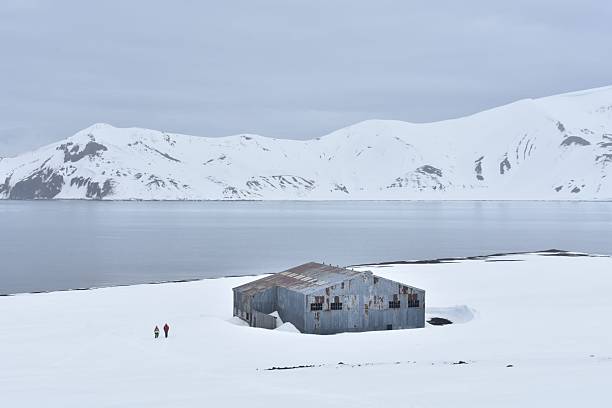 istock Abandoned Shack in Snowy Antarctic Landscape with Explorers by the Shoreline 2217590192