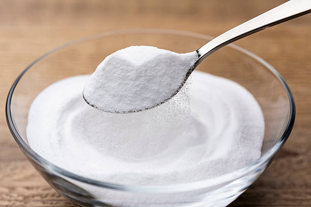 istock Scooping Baking Soda Powder from Glass Bowl on Wooden Table 2217593759