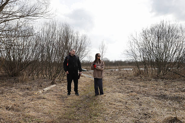 istock Two adults enjoying a peaceful outdoor break during an overcast day, positioned in a desolate early spring meadow with bare trees and a wetland shoreline in the background. 2217598965
